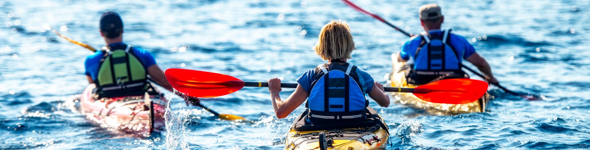 Three people kayaking on an open river.