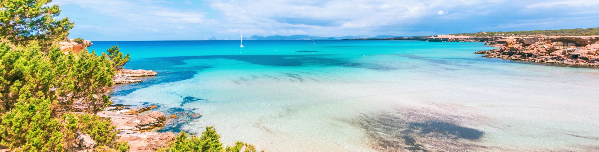 A beautiful sandy beach covered in shallow bright blue water and half surrounded by stone walls.