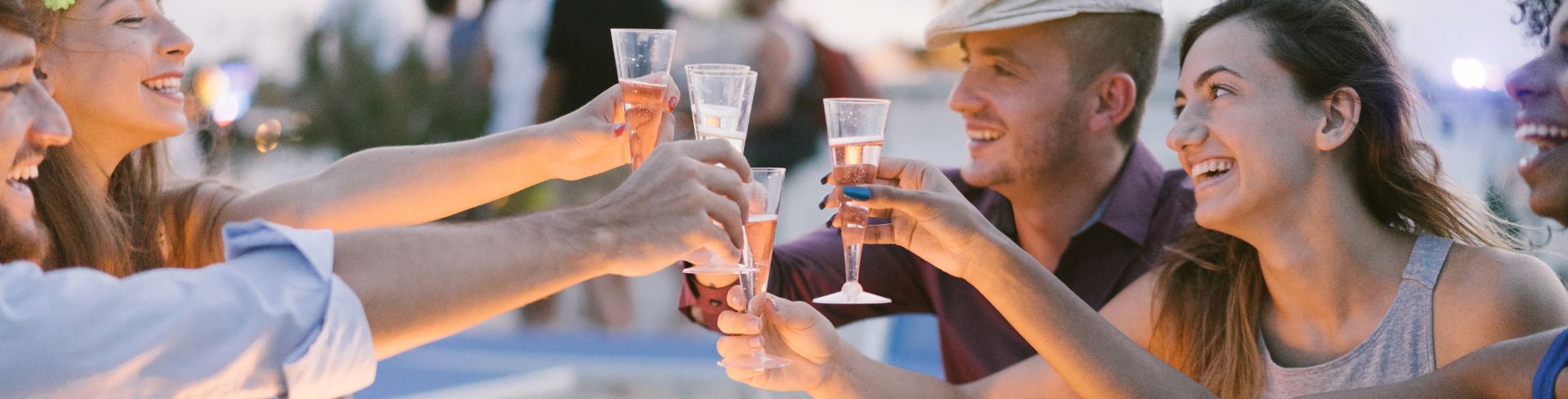 Five friends sitting at a small table on the beach toast with flutes of champagne. 