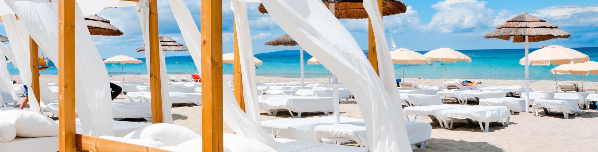 A four poster canopy bed on a beach facing towards the ocean, surrounded by other beds and beach loungers.