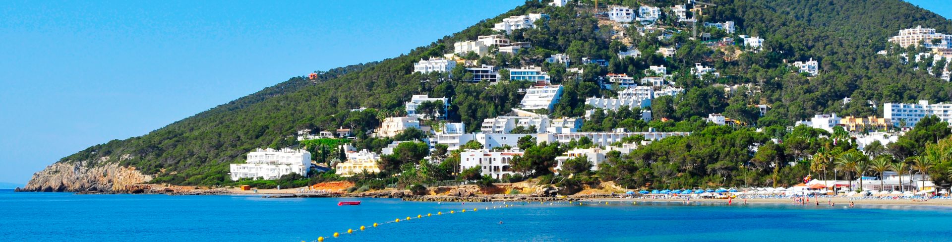 Bright blue water with a green hill in the background populated with white houses.