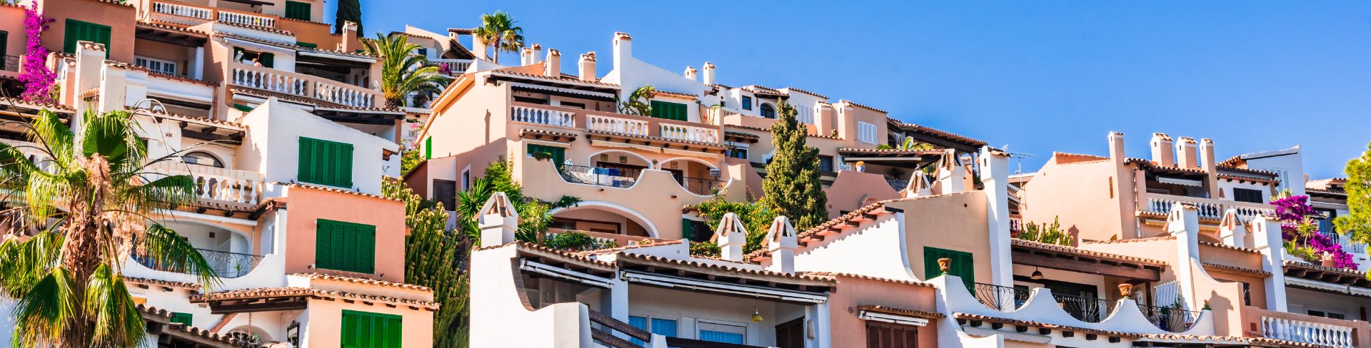 Rows of homes built into a hill and decorated in whites and pastels with Spanish tile roofs.