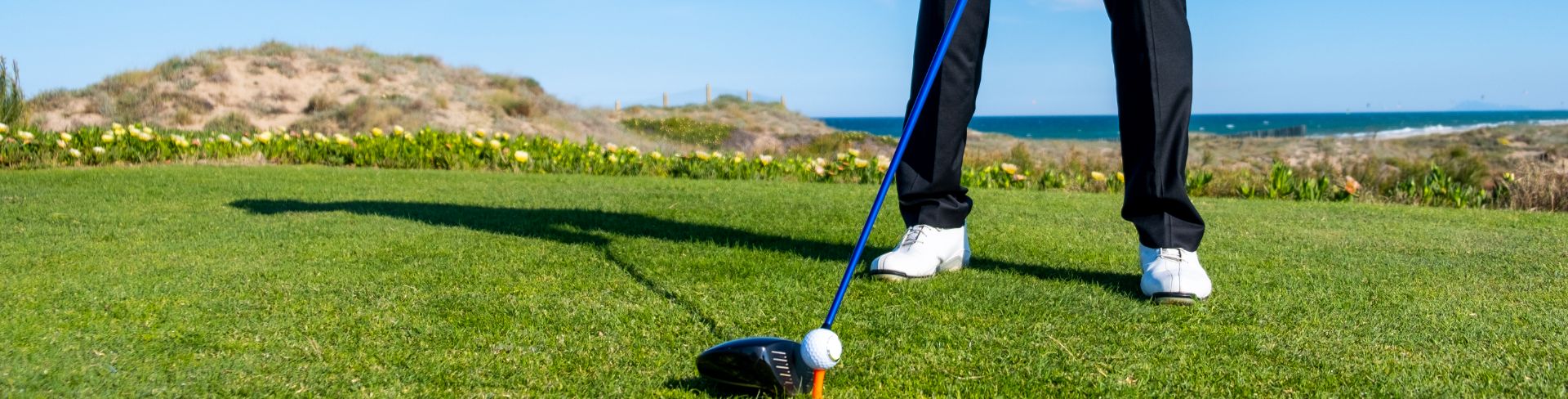 A person stands on a golf course, lining up their club with the golf ball on the tee.