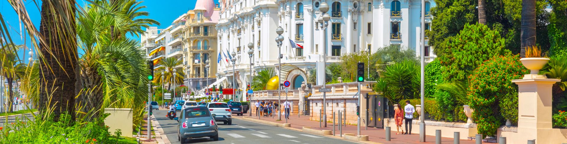 A promenade during a sunny day featuring palm trees and old French architecture.