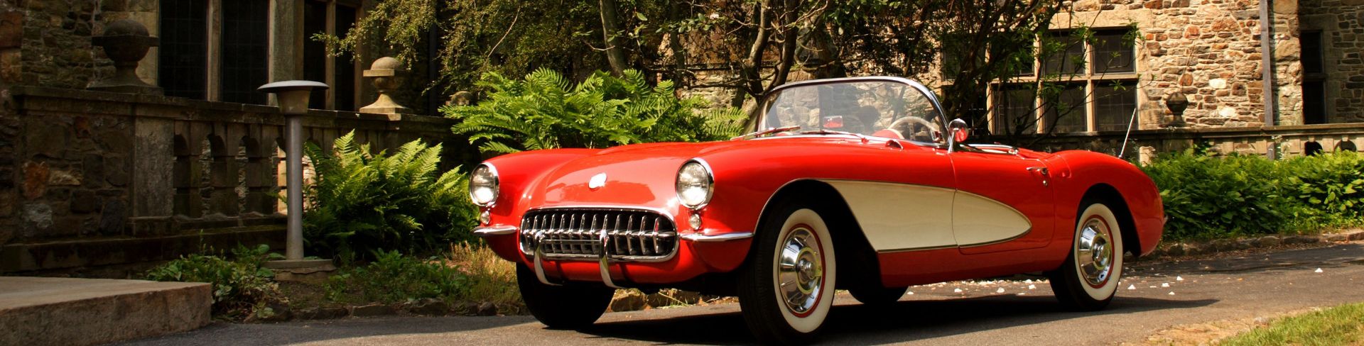 A red vintage car parked in the driveway of a stone mansion.