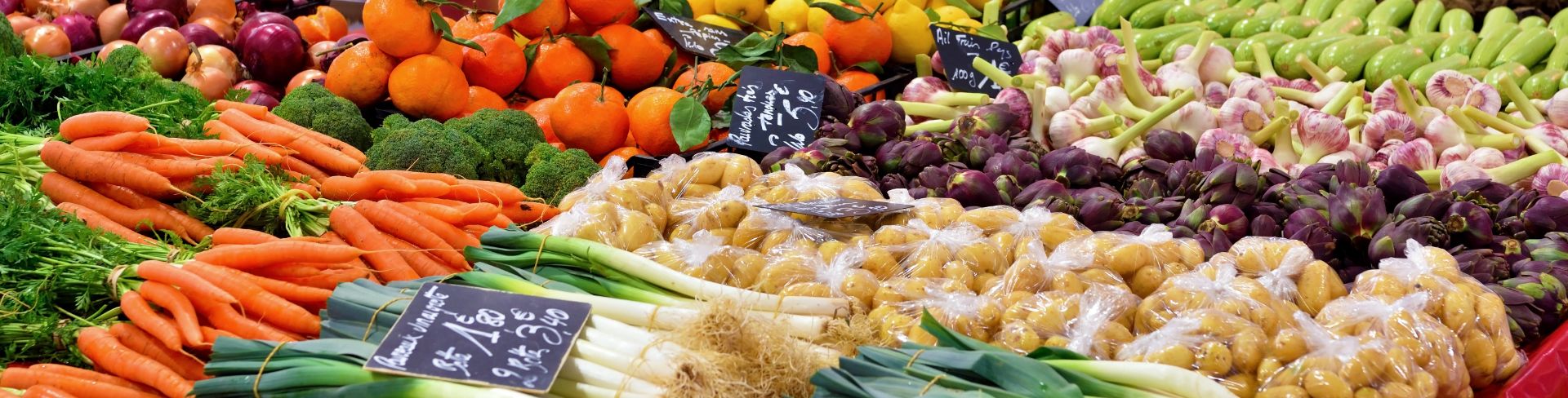 A table at a market full of fresh produce such as scallions, carrots, potatoes, broccoli and more.