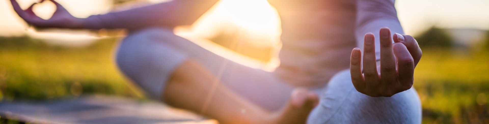 A person sits cross legged on a mat with hands resting on their knees and facing upwards.