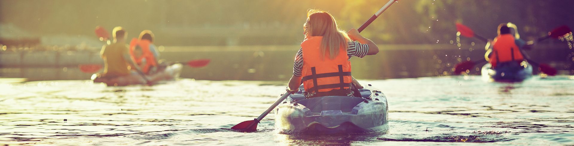 A group of kayakers paddling on a body of water into the sunset.