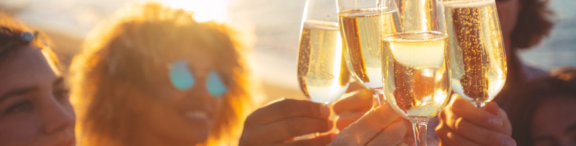 A group of people toast with flutes of sparkling wine at sunset.