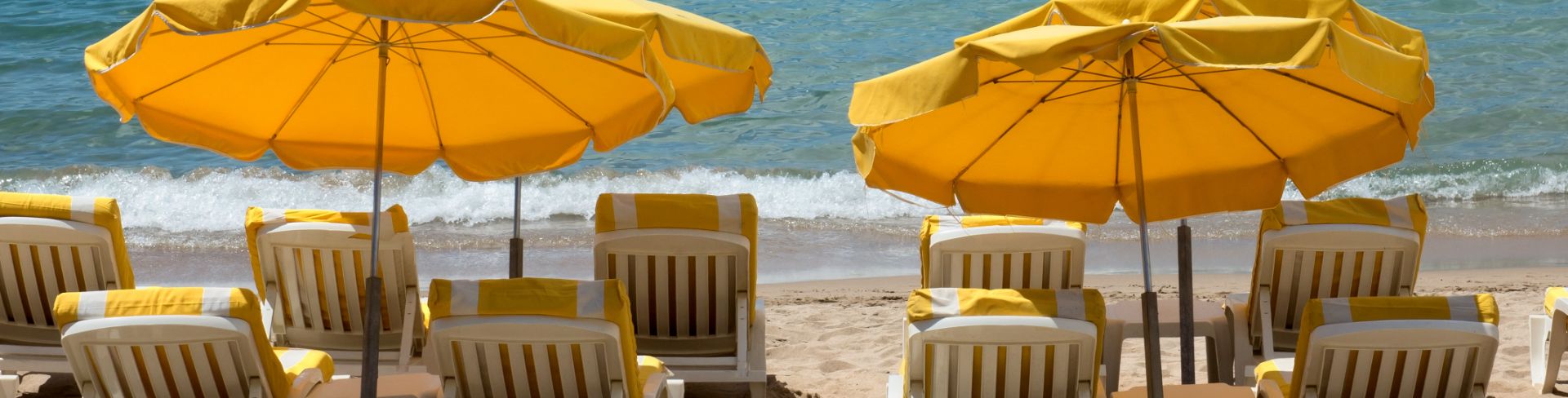Beach lounge chairs facing the ocean and shaded by a matching yellow umbrellas.