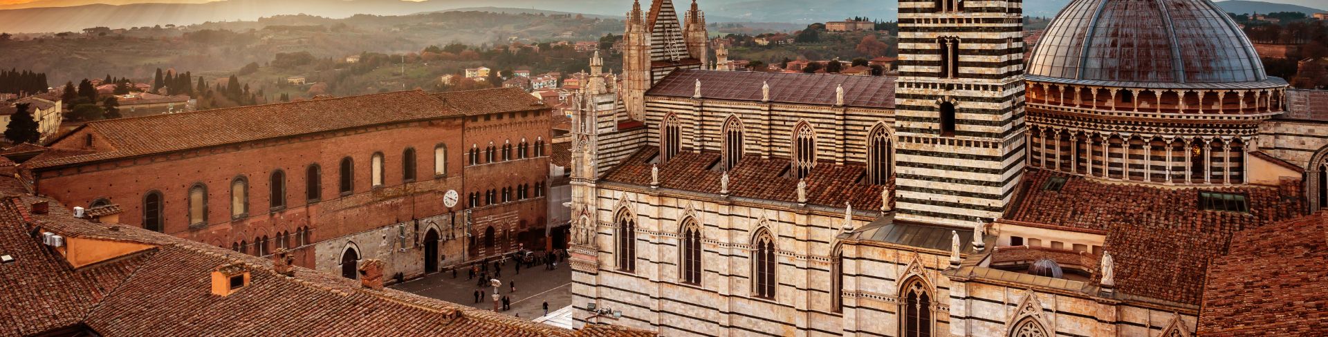 A Romanesque cathedral with a tall striped tower and large dome in the glow of a sunset.