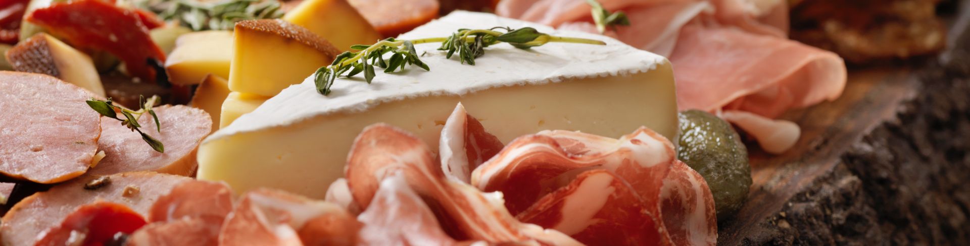 A charcuterie and cheese board full of cured meats, cheeses, olives and herbs.