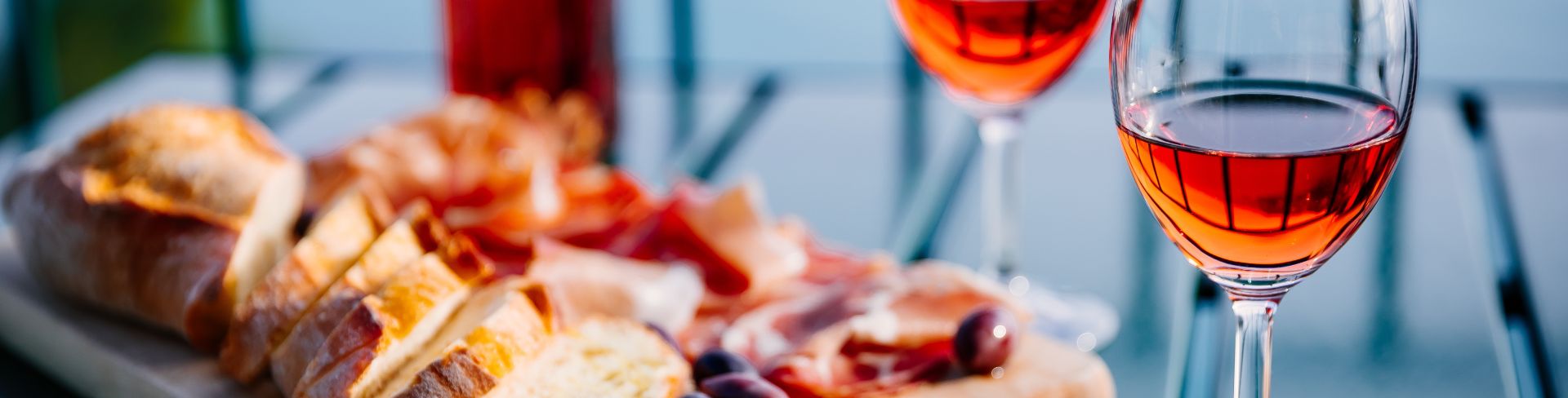 Two glasses of orange wine sit on a table next to a charcuterie board with a view of the sea in the background.