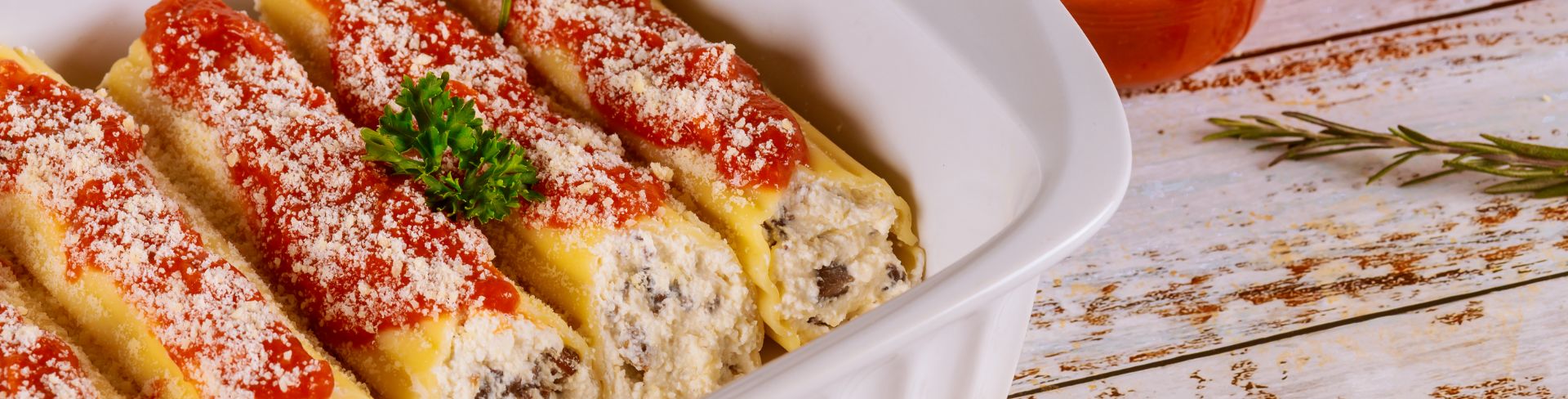 A baking dish of cannelloni pasta stuffed with ricotta, mushrooms and tomato sauce.