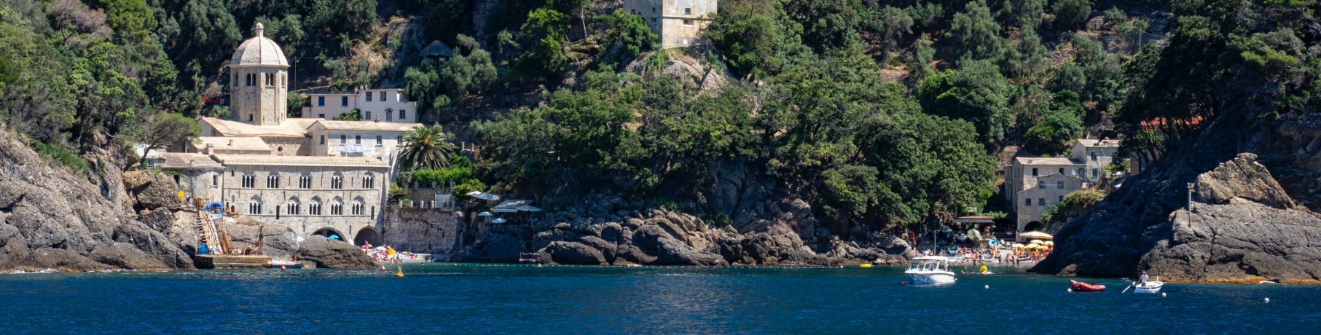 An old stone monastery built into a green hillside overlooking the Ligurian Sea.