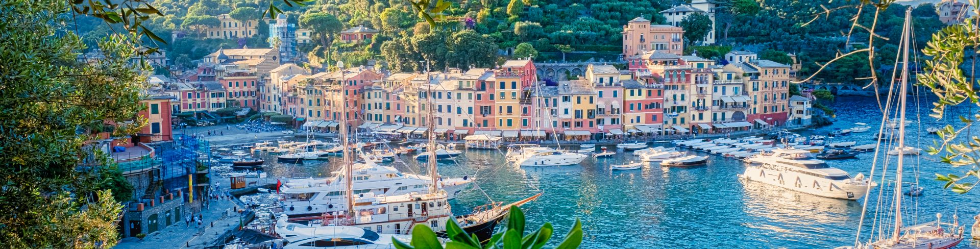 The view of Portofino harbor where yachts are at anchor and pastel buildings stand on the edge.