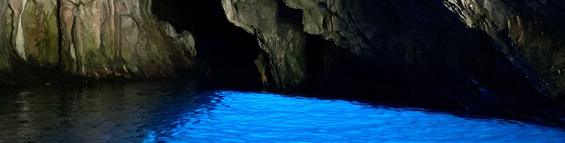 A look inside the Blue Grotto at the bright blue water and cave walls.