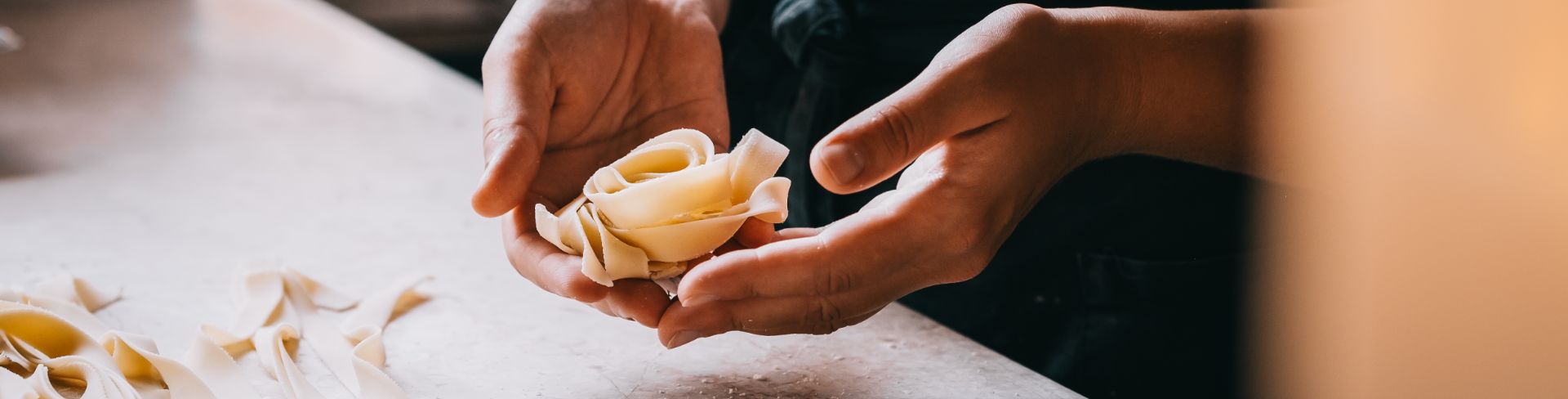 A chef's hands hold a bundle of freshly made pasta in a kitchen.