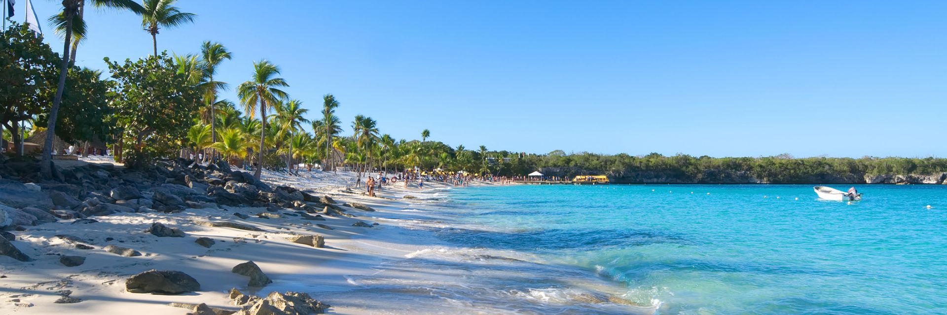 Turquoise blue waves wash up on a white sand beach lined with palm trees.