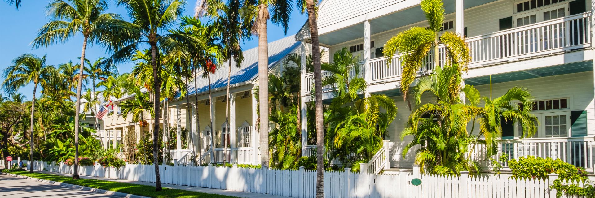 A row of classic conch homes in Key West showing front porches shaded by palm trees.