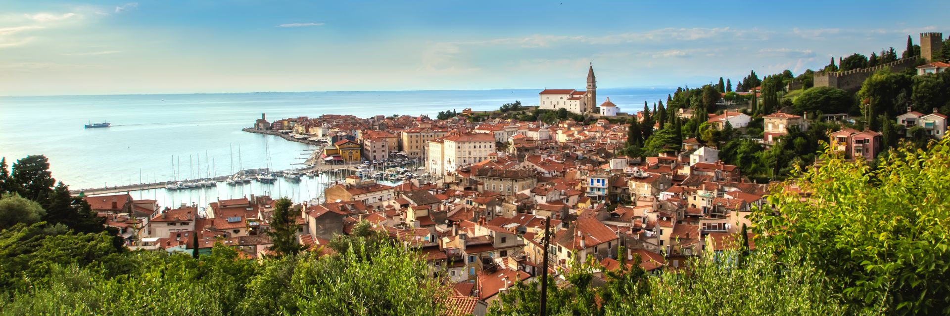 Bright blue water behind an orange-roofed town and green trees.