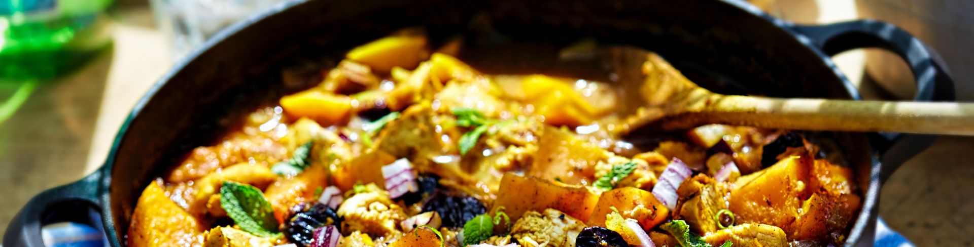 A cast iron skillet of a Moroccan stew consisting of fried chicken, pumpkin, cherries and red onion.