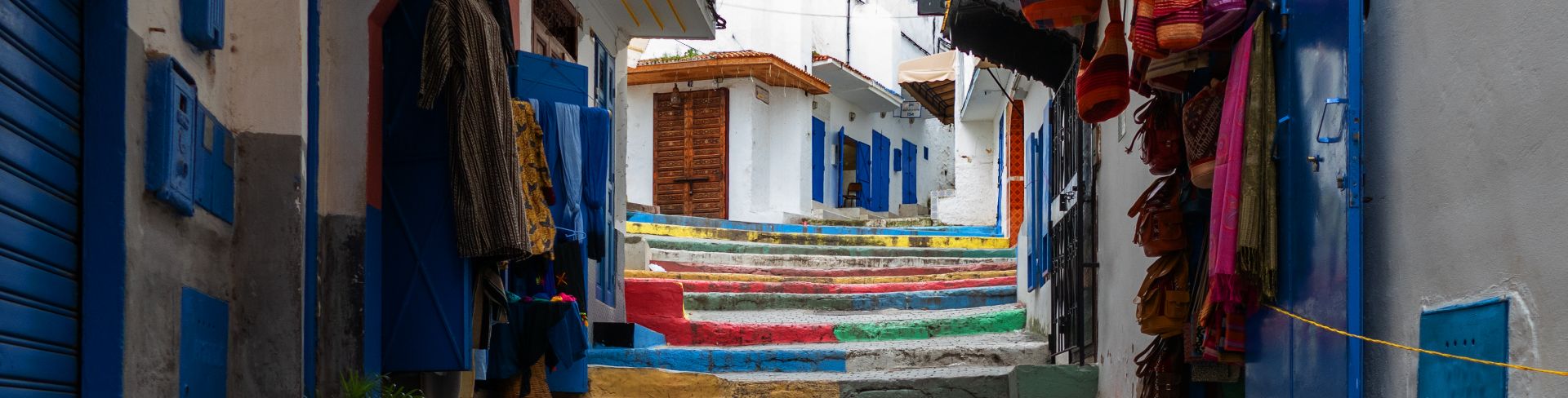 Multicolored steps in a narrow alleyway surrounded by whitewashed buildings with blue doors and shutters.
