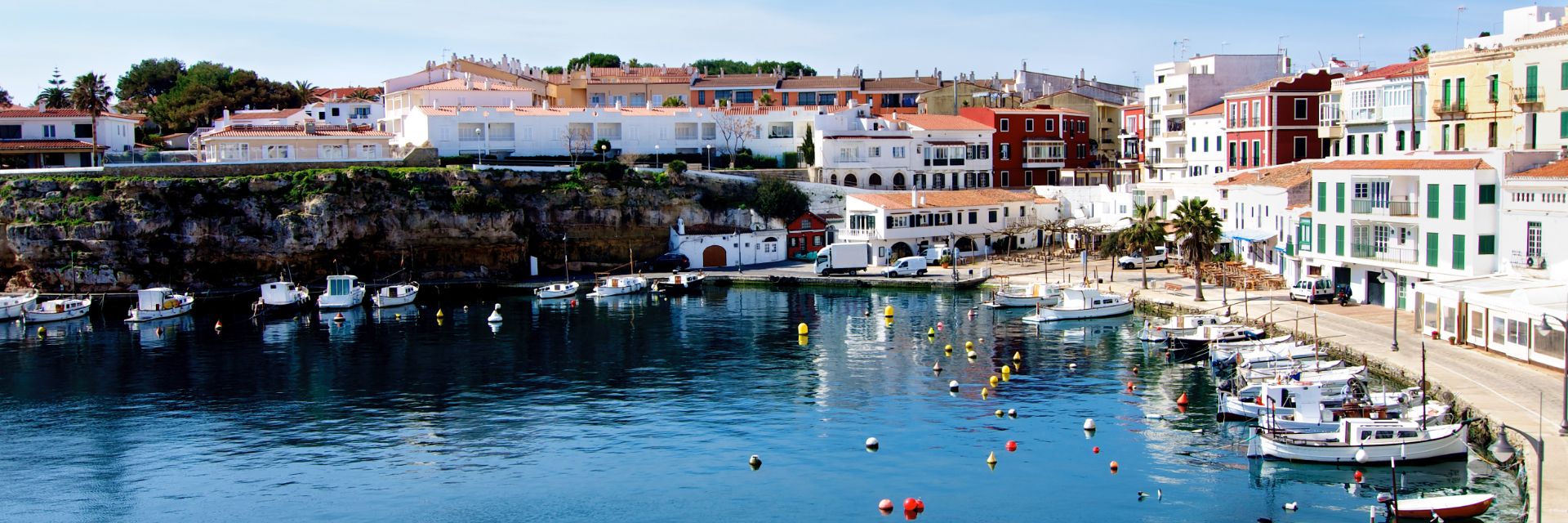 A small harbor with white fishing boats at anchor, surrounded by a Mediterranean town.