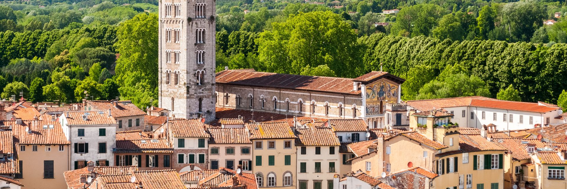The aerial view of an old Italian town with terracotta roofs, green shutters and a bell tower.