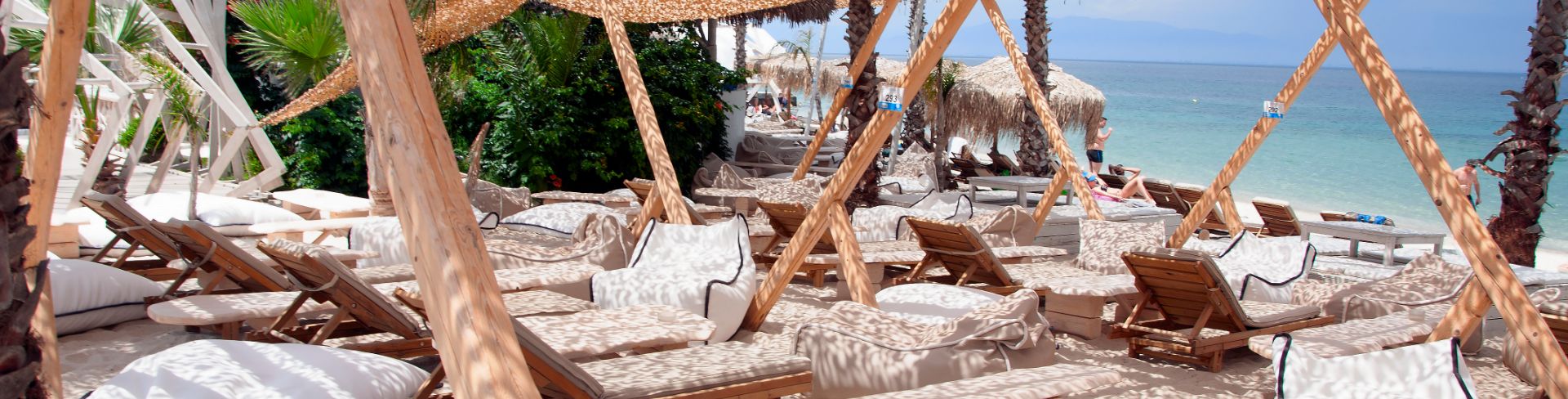 A sunbathing area set up on a white-sand beach with lounge chairs under a natural hatch shade awning.