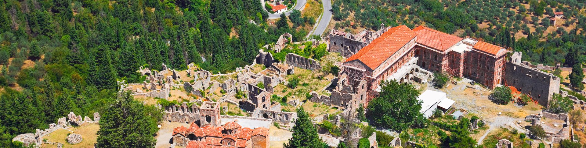 The ruins of an old town in Mystras, Greece, surrounded by a green forest.