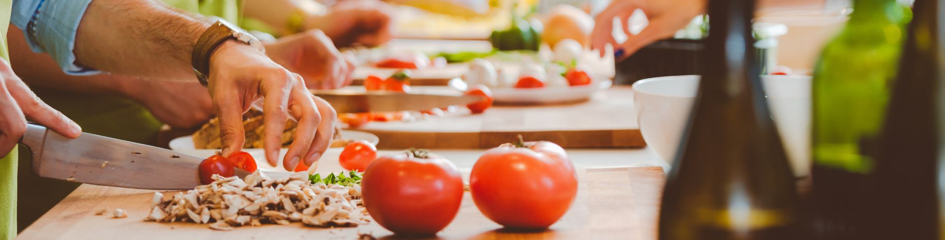 Chefs slicing tomatoes on a wooden chopping board.