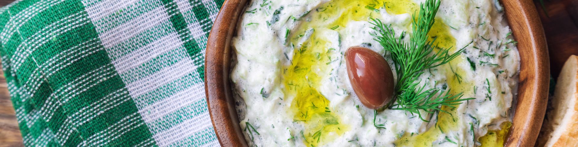 The top-down view of tzatziki sauce in a bowl topped with an olive and fresh dill.
