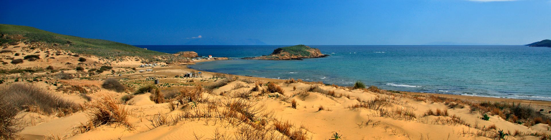  Golden sand dunes dotted with patches of grass and small azure waves lap at the shore.