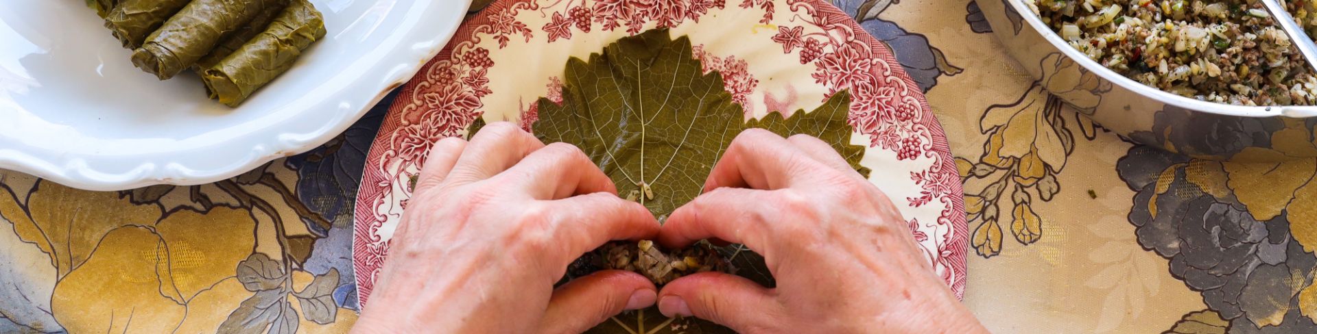 A pair of hands stuffs and rolls grape leaves with a rice mixture.