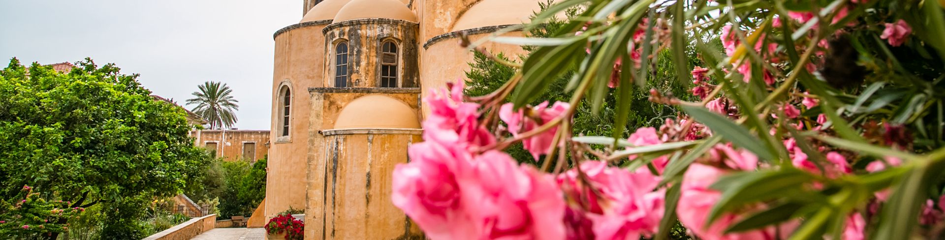 An old monastery in Chania, on the island of Crete, Greece, framed by pink flowers in the foreground.