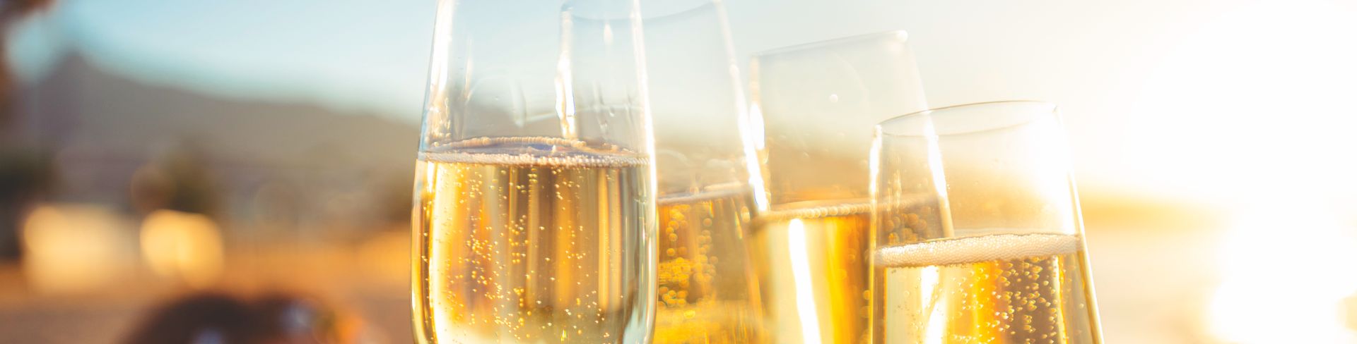 A group of friends toast with flutes of sparkling wine on a beach at sunset.