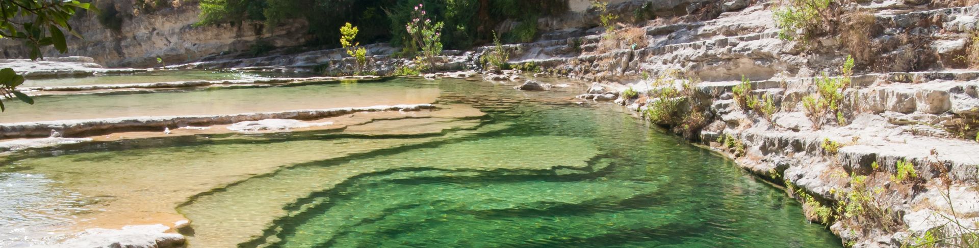 A natural pool in Cavagrande Reserve full of blue-green water and greenery on a hill in the background.