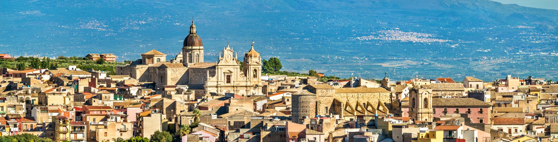 Panoramic view of an old Italian city with Mount Etna in the background.