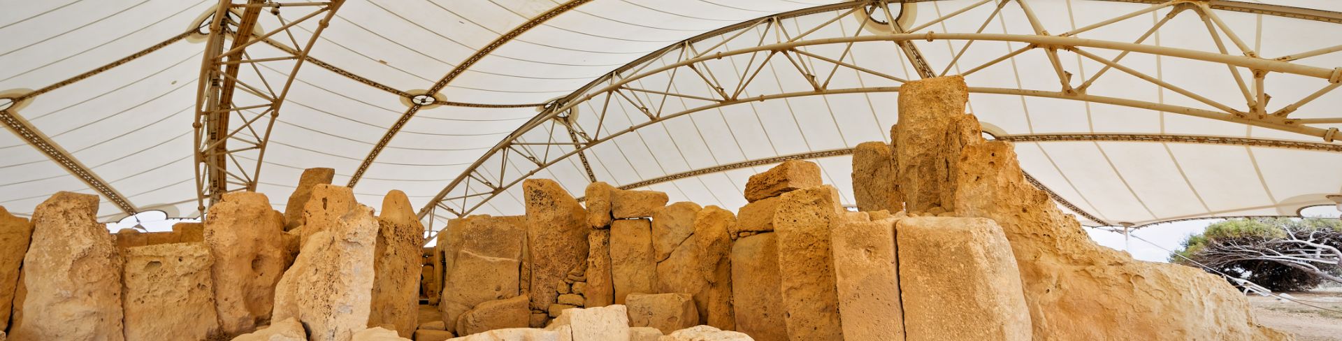 The ruins of megalithic temples made of large limestone blocks under a protective awning.