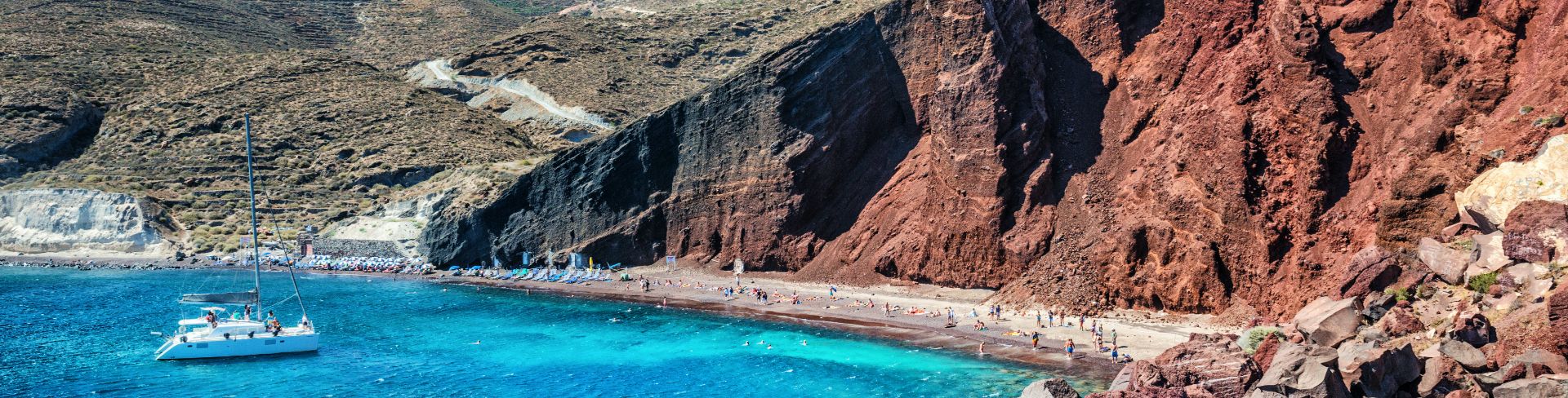 Beach goers sit in front of the rocky coast line.