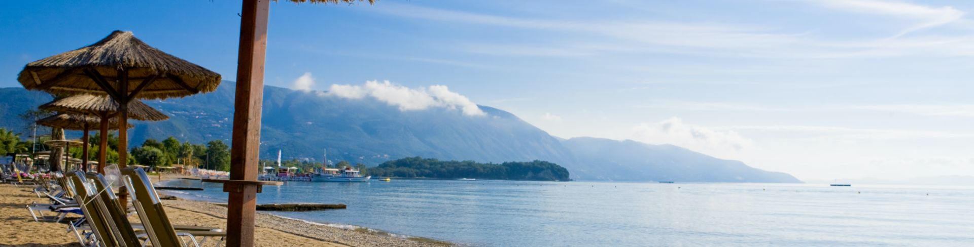 Beach chairs look out at the transparent sea with mountains in the distance.