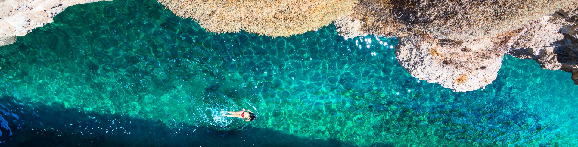 An aerial view of a woman swimming in the green waters of Milos.