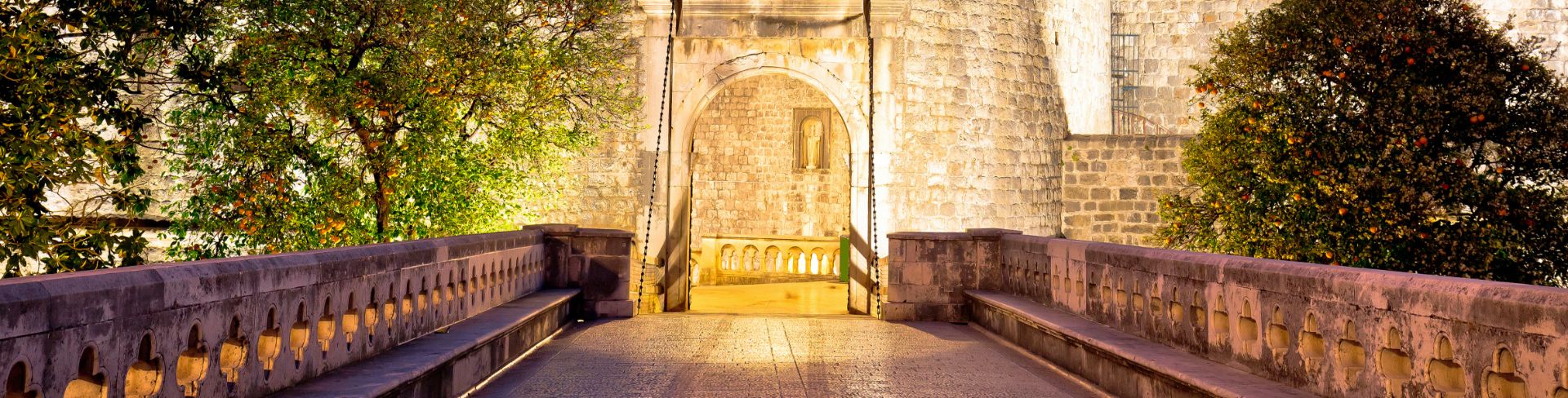  Illuminated in the night, a bridge leads to a fortress's entrance.