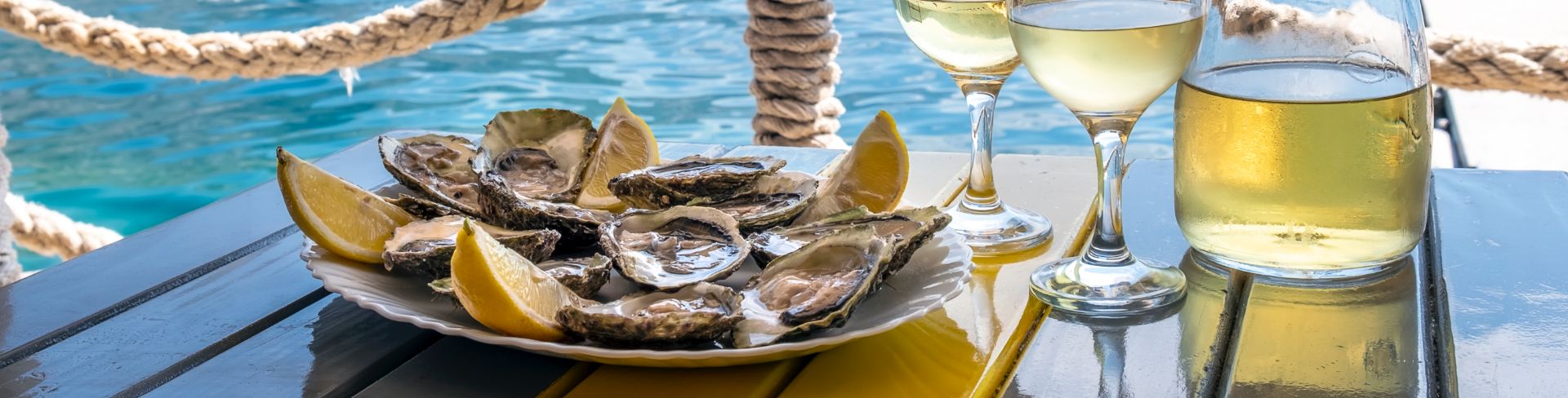 White wine and a plate of oysters sit next to blue waters, waiting to be enjoyed.