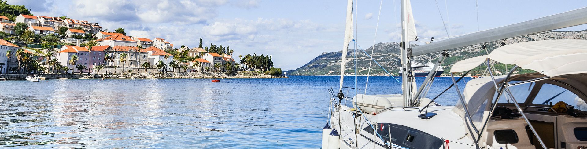 Clouds litter the blue sky over a sailboat in the blue water.