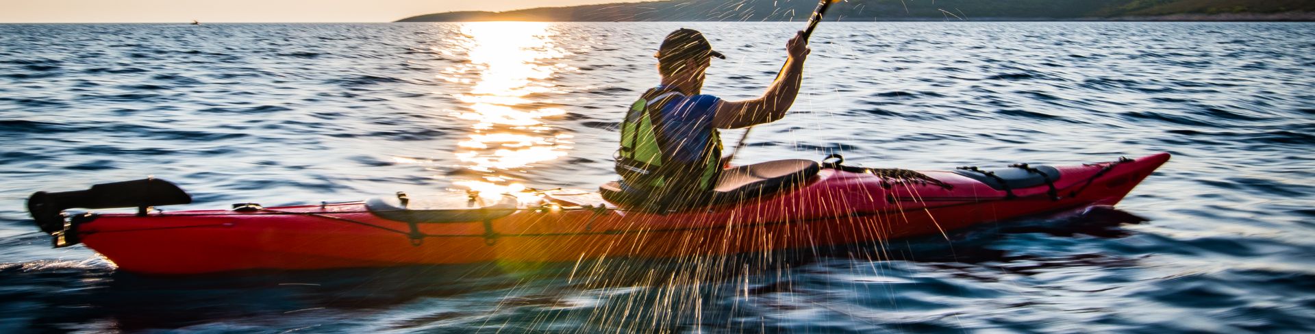 A man kayaks in the setting sun.