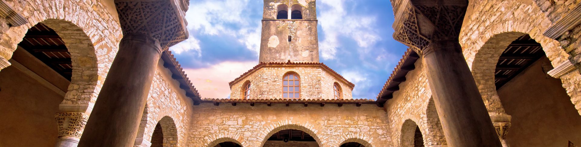 Columns frame a bell tower rising towards the blue cloud-filled sky.
