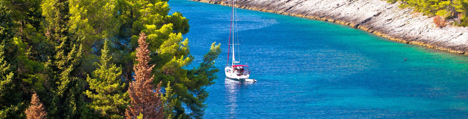 A single sailboat navigates through a channel of blue-green water.