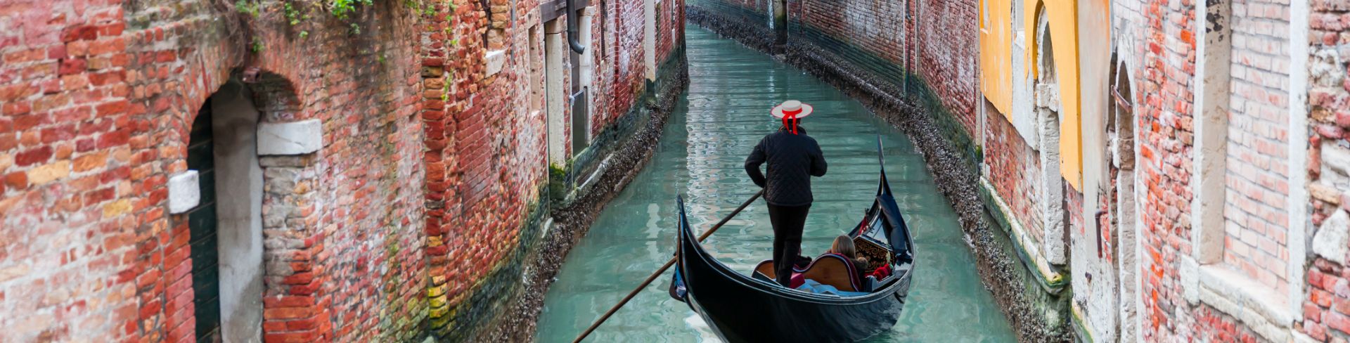 A gondolier navigates through a brick-lined canal.